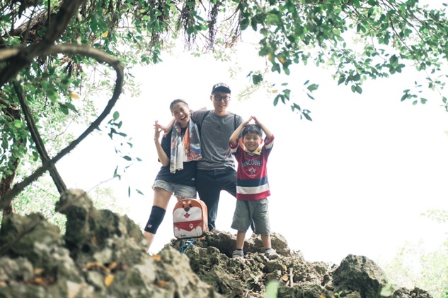 一家三口在戶外登山健行，站在岩石上開心合影，周圍環繞著綠意盎然的樹木。